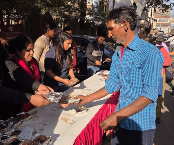 NCF volunteer handing a foil-packaged hot meal to a beneficiary on the street