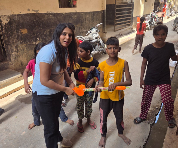 Volunteer handing a large bubble wand toy to a boy in a narrow residential alley