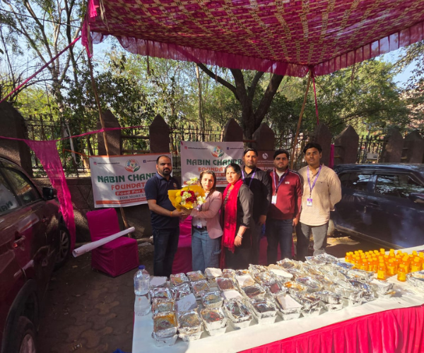 NGO members and sponsors posing with a bouquet beside foil meal containers ready for distribution