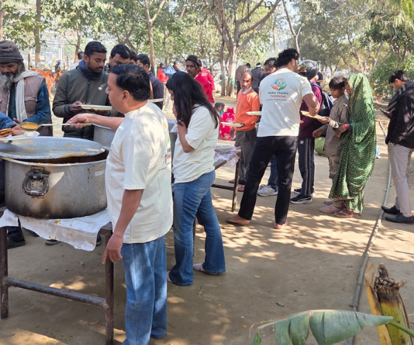 People queuing for meals served from a large pot in a park setting