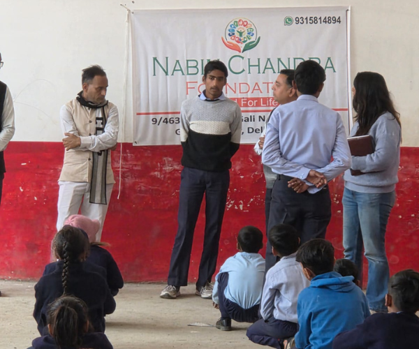 Foundation team standing before a banner addressing children seated on the floor
